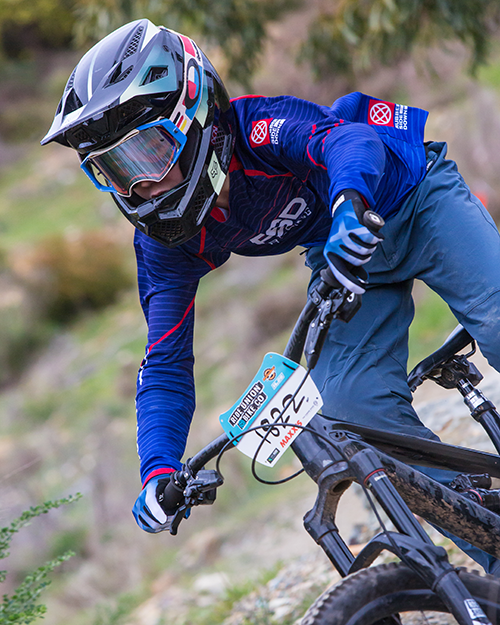 Racer in a blue RSD jersey and full face helmet dropping into a steep section with a race plate on the bars