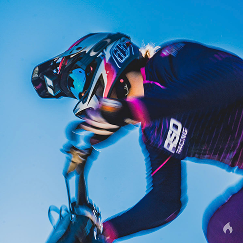 Close up of a rider in an RSD Racing jersey and full face helmet at speed against a blue sky