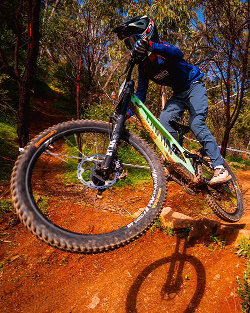 Downhill rider in an RSD jersey leaning a bike through a red dirt corner on a taped race track